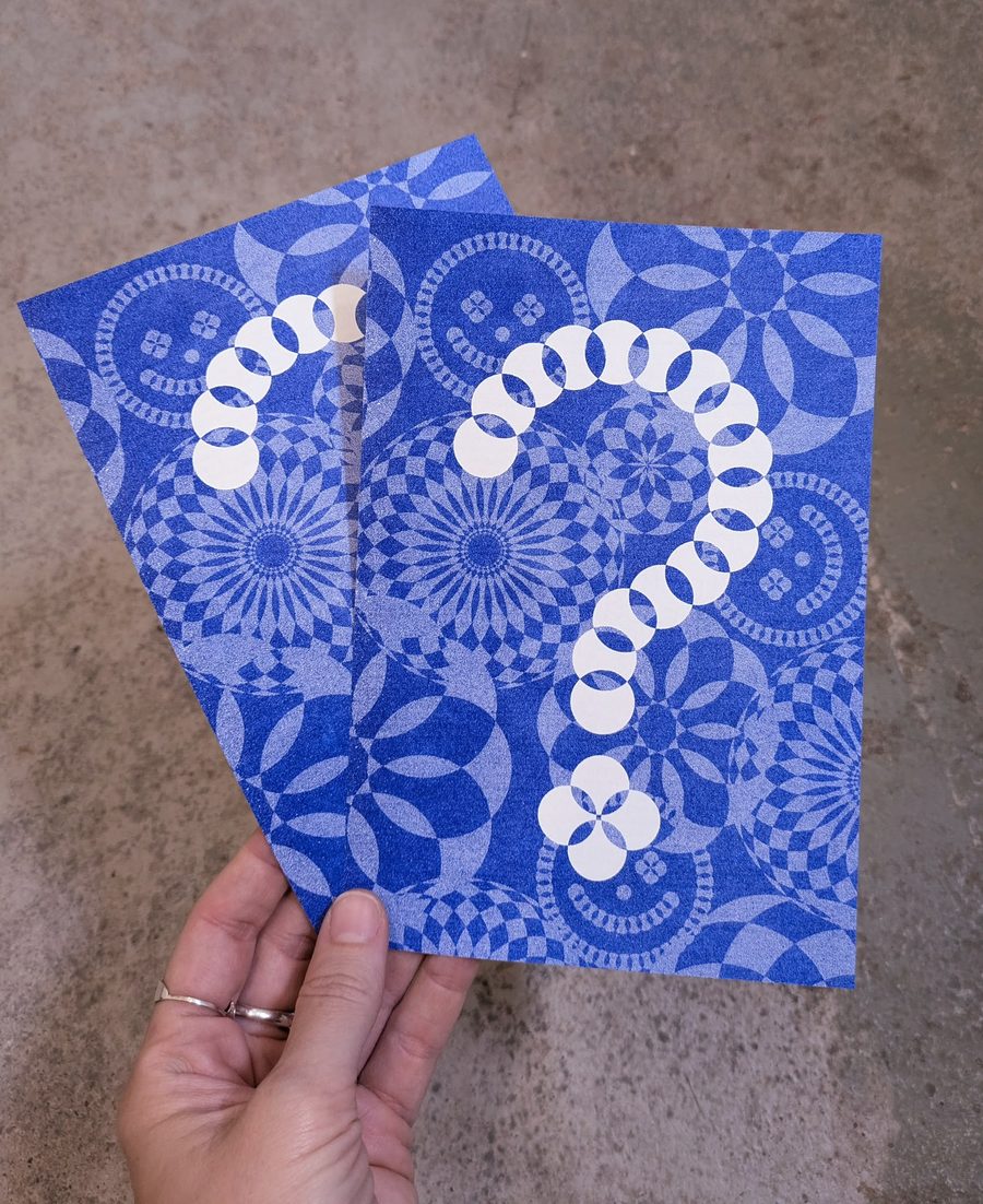 Mão a segurar dois flyers do festival, impressos em azul com o padrão gráfico do Vaudeville Rendez-Vous.