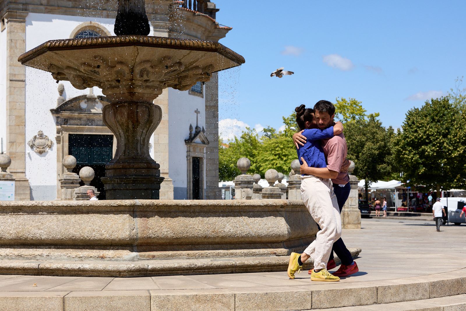 Dois artistas de circo abraçados durante um espetáculo junto a um chafariz, numa praça, no Festival Vaudeville Rendez-Vous 2026.